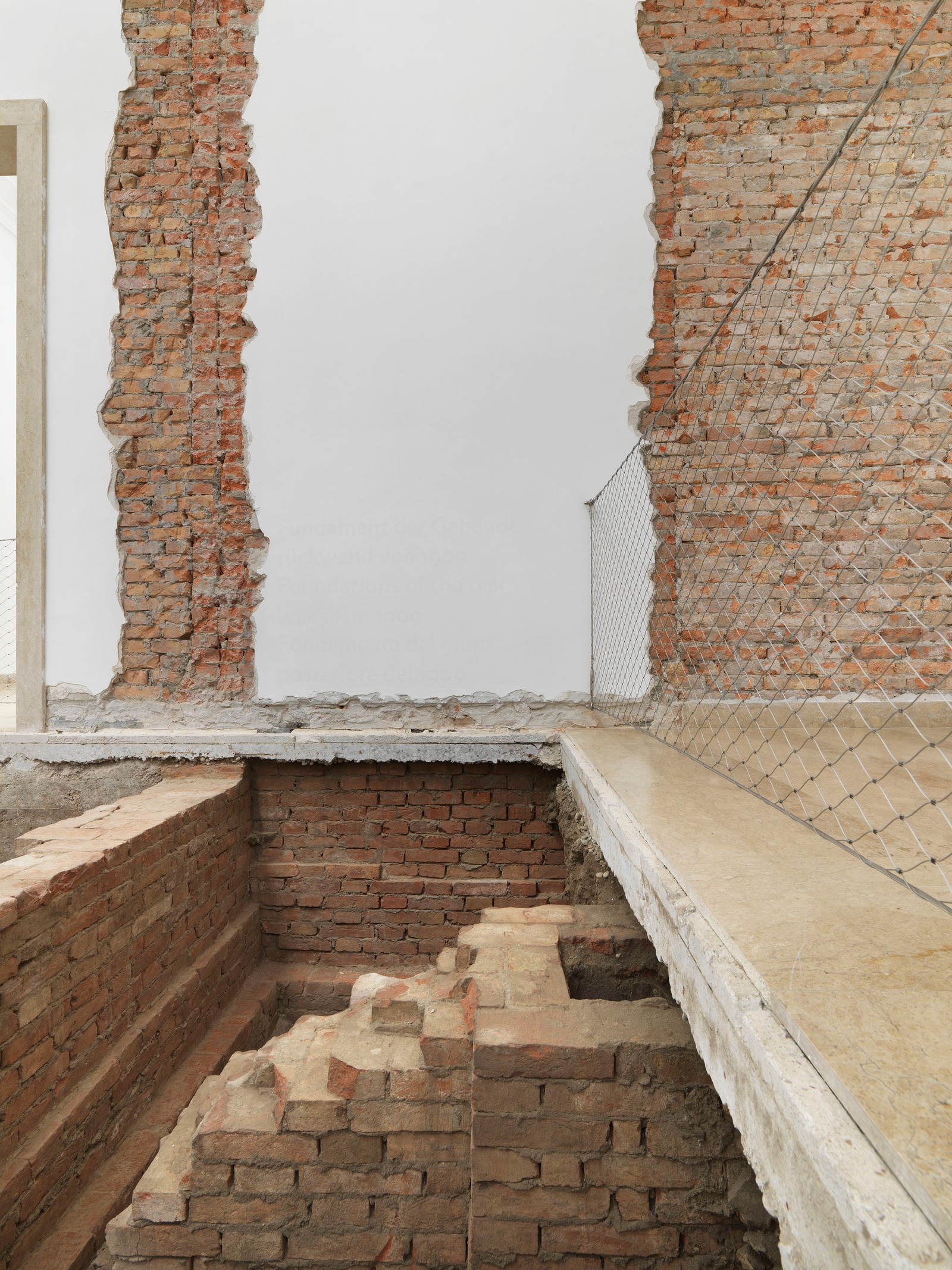 Maria Eichhorn, Relocating a Structure. German Pavilion 2022, 59th International Art Exhibition – La Biennale di Venezia, 2022, detail: Foundations of the rear wall from 1909; rear wall of the building from 1909, interior wall from 1938, demolished in 1964; wall lettering; chimney from an earlier building (undated); doorway to the right side room from 1909, walled up in 1912, exhibition view, © Maria Eichhorn / VG Bild-Kunst, Bonn 2022, photo: Jens Ziehe